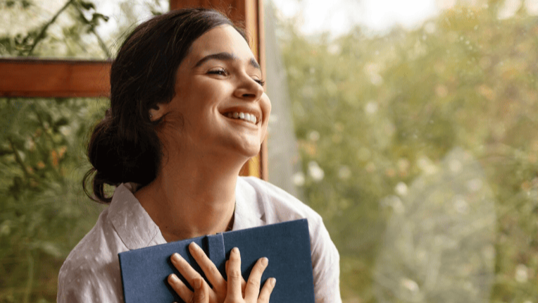 Mujer sonriente abrazando un libro, representando el vínculo entre lectura e inteligencia emocional
