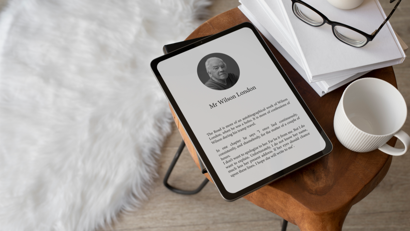 Tablet sobre mesa de madera mostrando un libro digital con el título "Mr Wilson London", junto a una taza blanca, unas gafas y una pila de documentos, en un ambiente acogedor con alfombra blanca